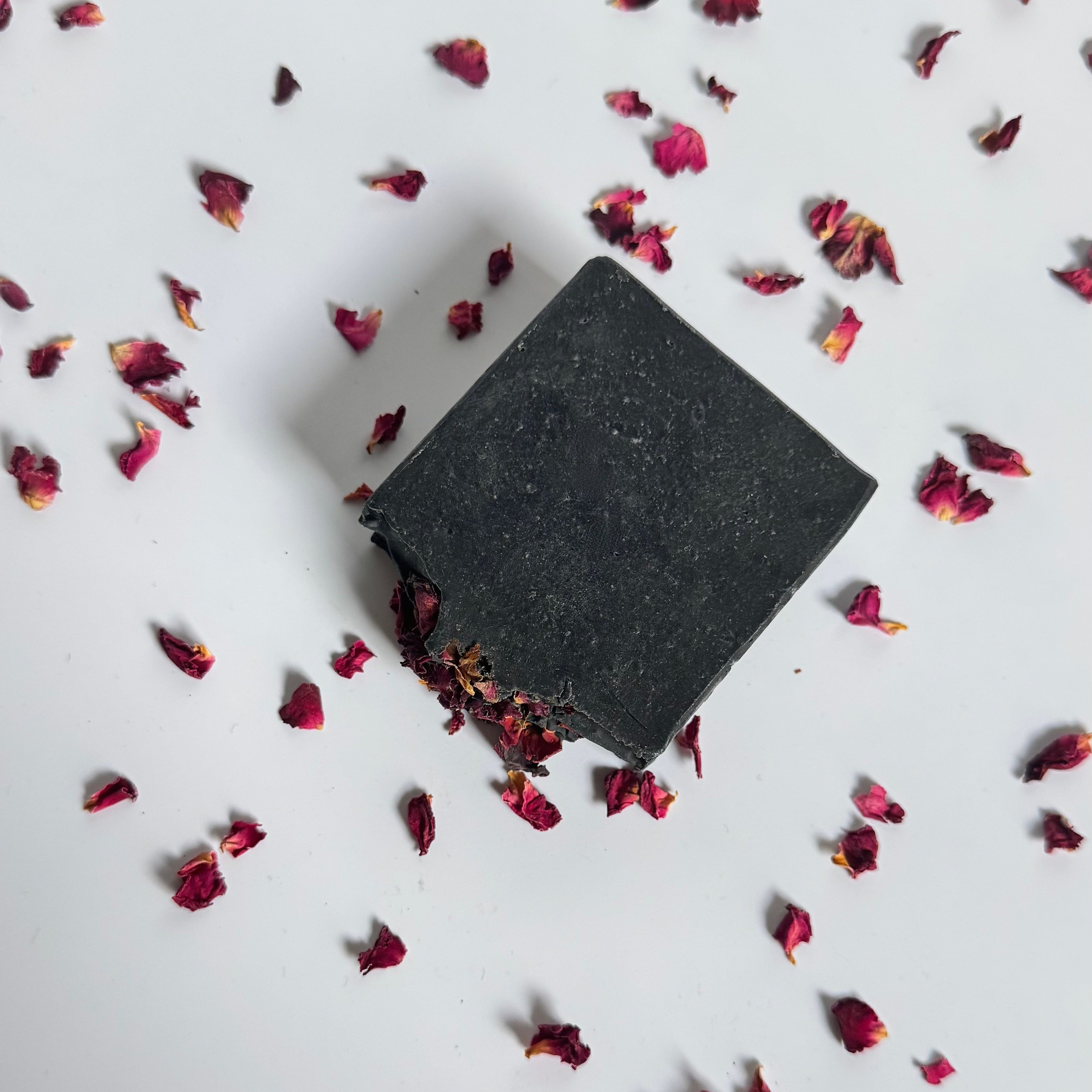 Black activated charcoal lavender tea tree natural soap bar with dried rose petals on a white background 
