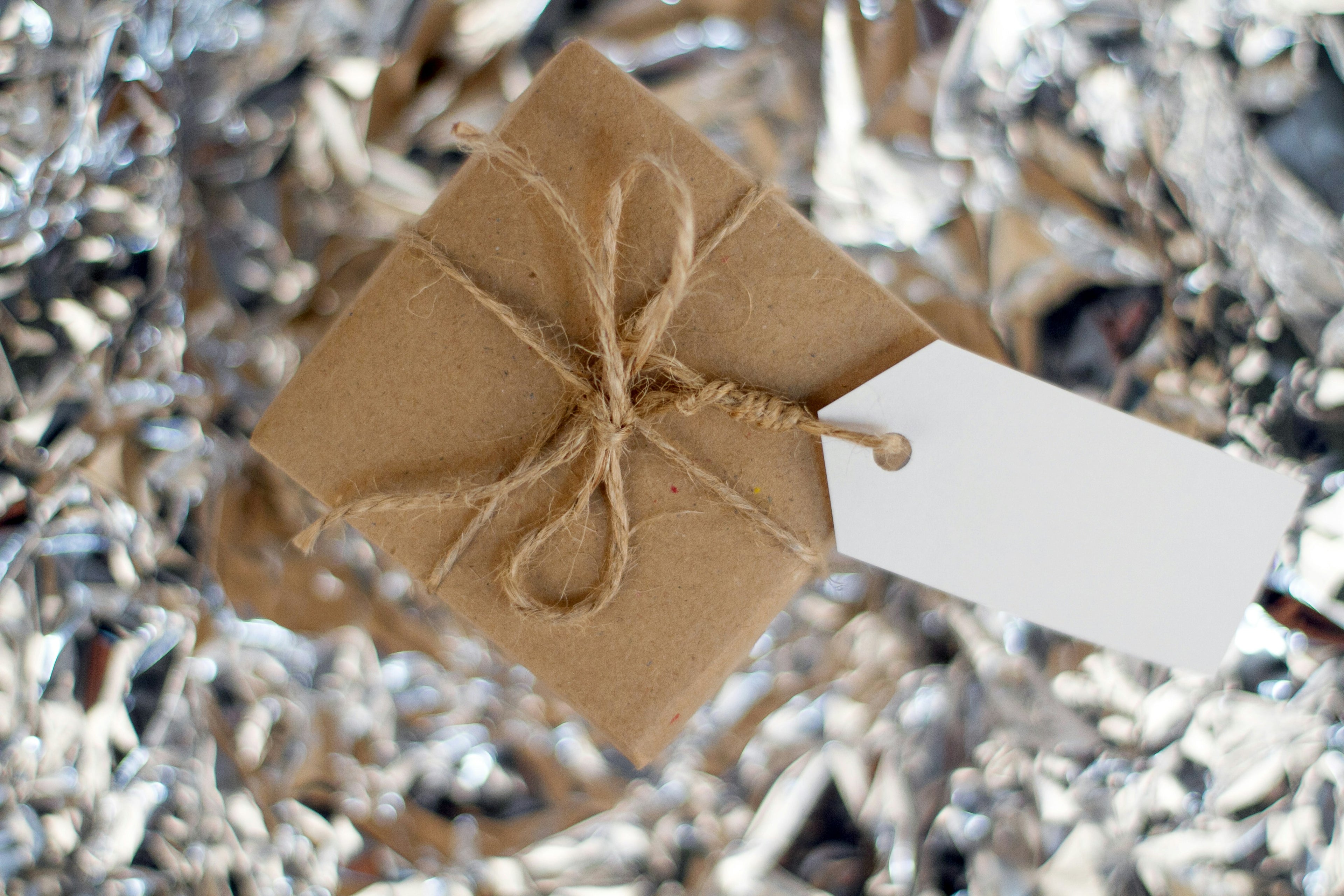Small brown gift box with string bow and white tag on shredded paper background
