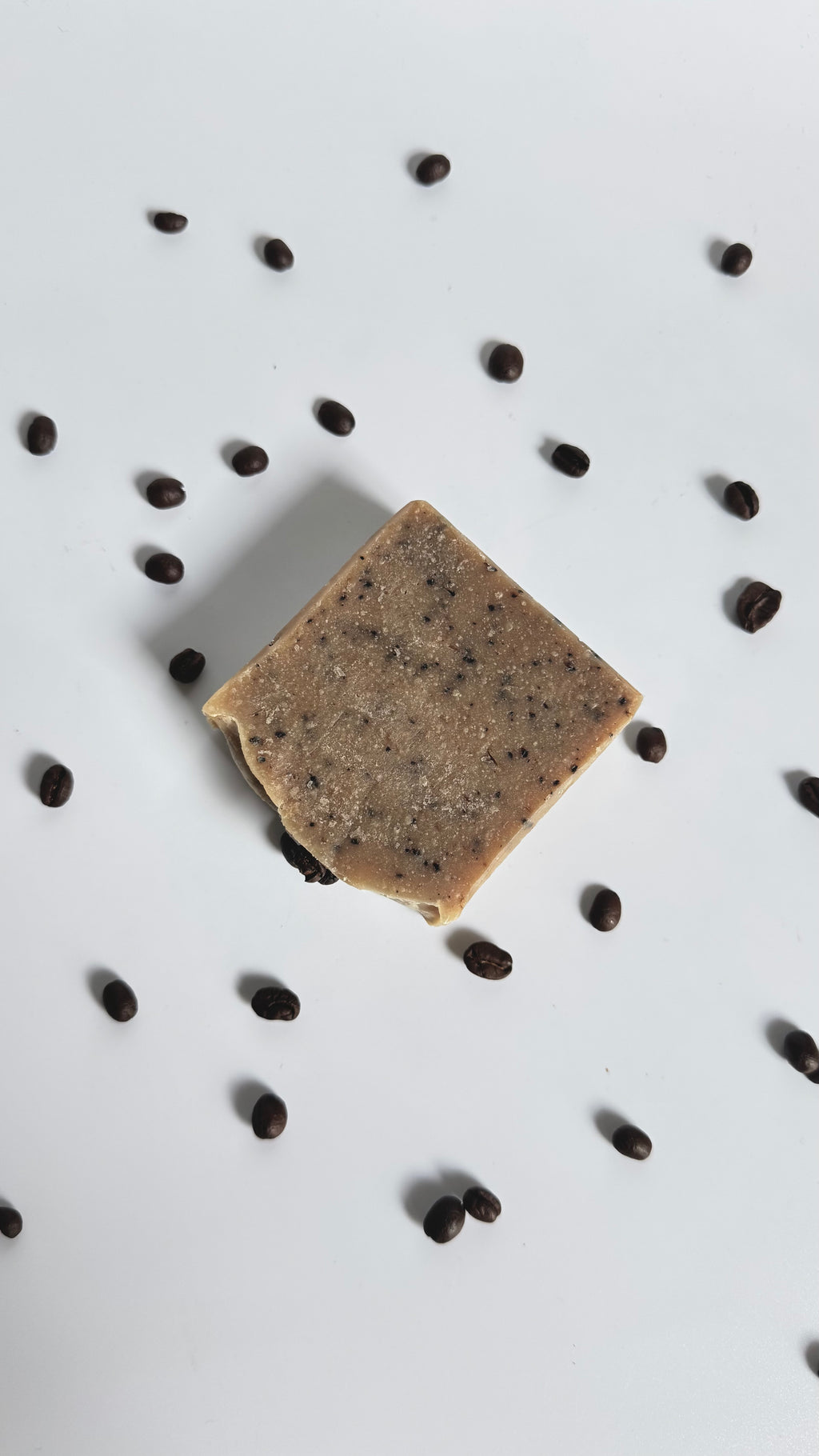 Brown coffee natural soap bar with coffee beans above view with dried jasmine flowers on a light gray background