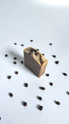 Brown coffee natural soap bars with coffee beans above side view with dried jasmine flowers on a light gray background