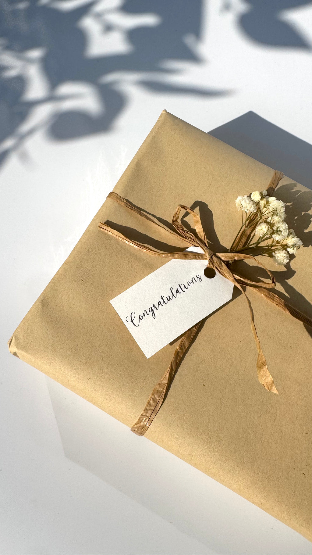 Gift wrapped in brown paper with a 'Congratulations' tag on a white surface.