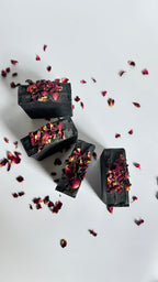 Four black activated charcoal lavender tea tree natural soap bars above view in circle with dried rose petals on a white background