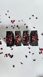 Four black activated charcoal lavender tea tree natural soap bars above view with dried rose petals on a white background