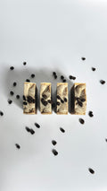 Four brown coffee natural soap bars with coffee beans above view with dried jasmine flowers on a light gray background
