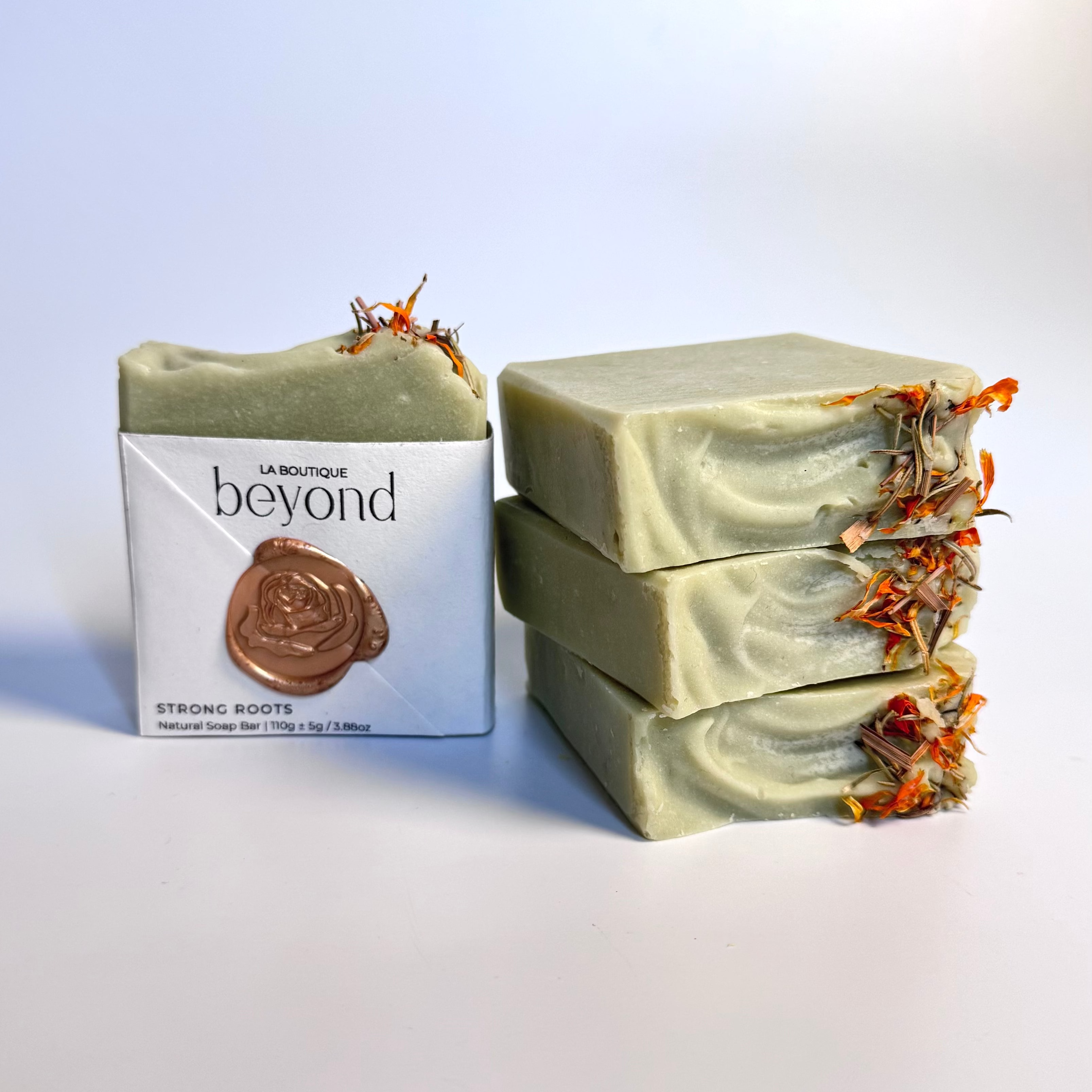 Four green rosemary cedarwood natural soap bars with dried floral botanical elements and a packaging labeled 'La Boutique Beyond' on a light background.