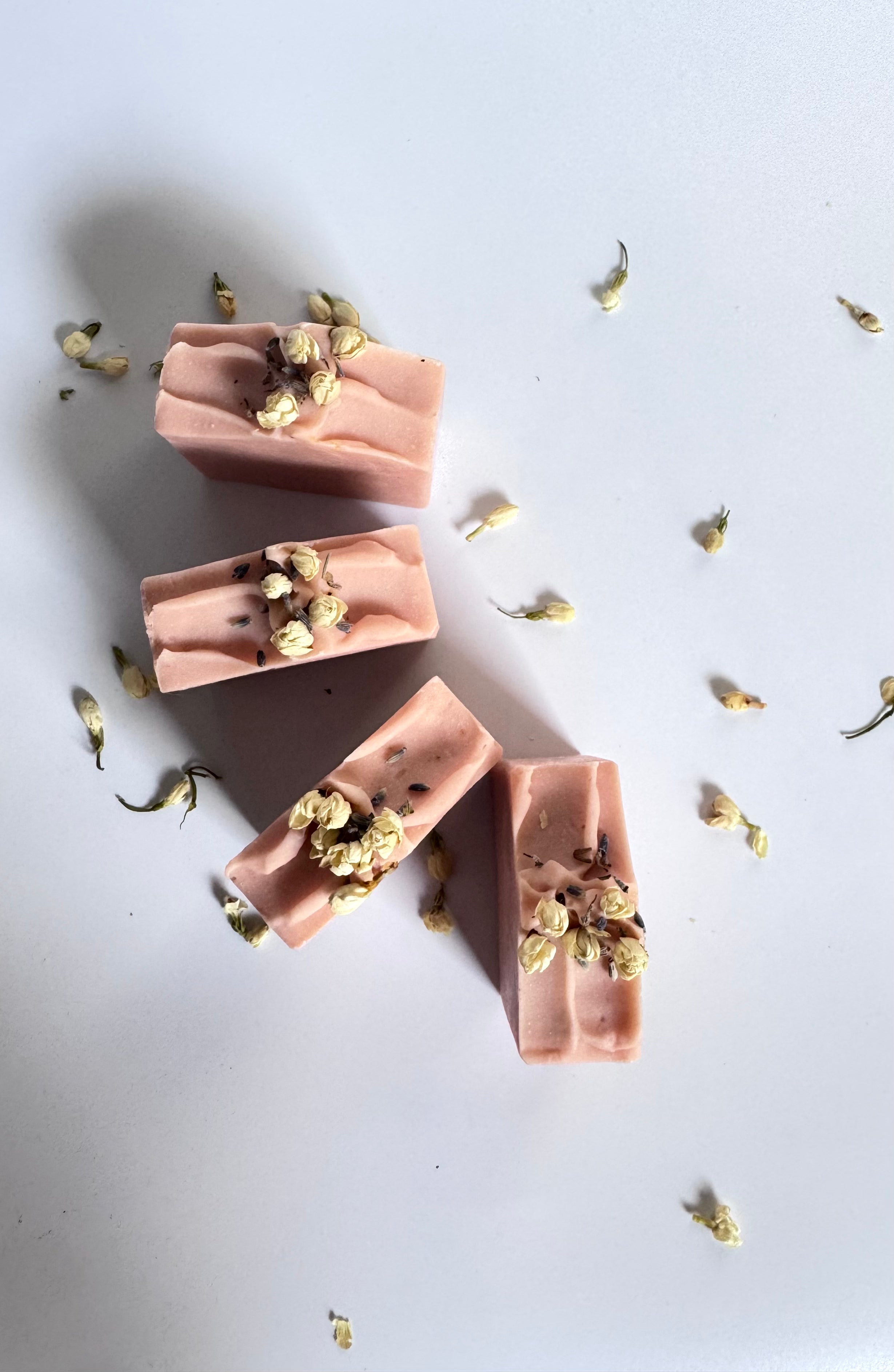 Four pink chamomile rose geranium natural soap bars in circle above view with dried jasmine flowers on a light gray background