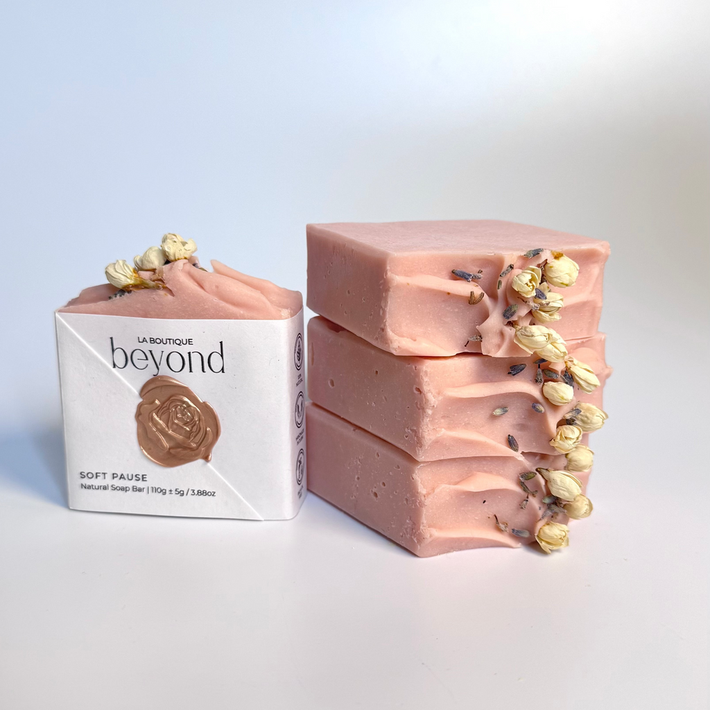 Stack of four pink chamomile rose geranium natural soap bars with dried jasmine flowers and a packaging labeled 'La Boutique Beyond' on a light background.