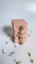 Stack of four pink chamomile rose geranium natural soap bars front view with dried jasmine flowers on a light gray background