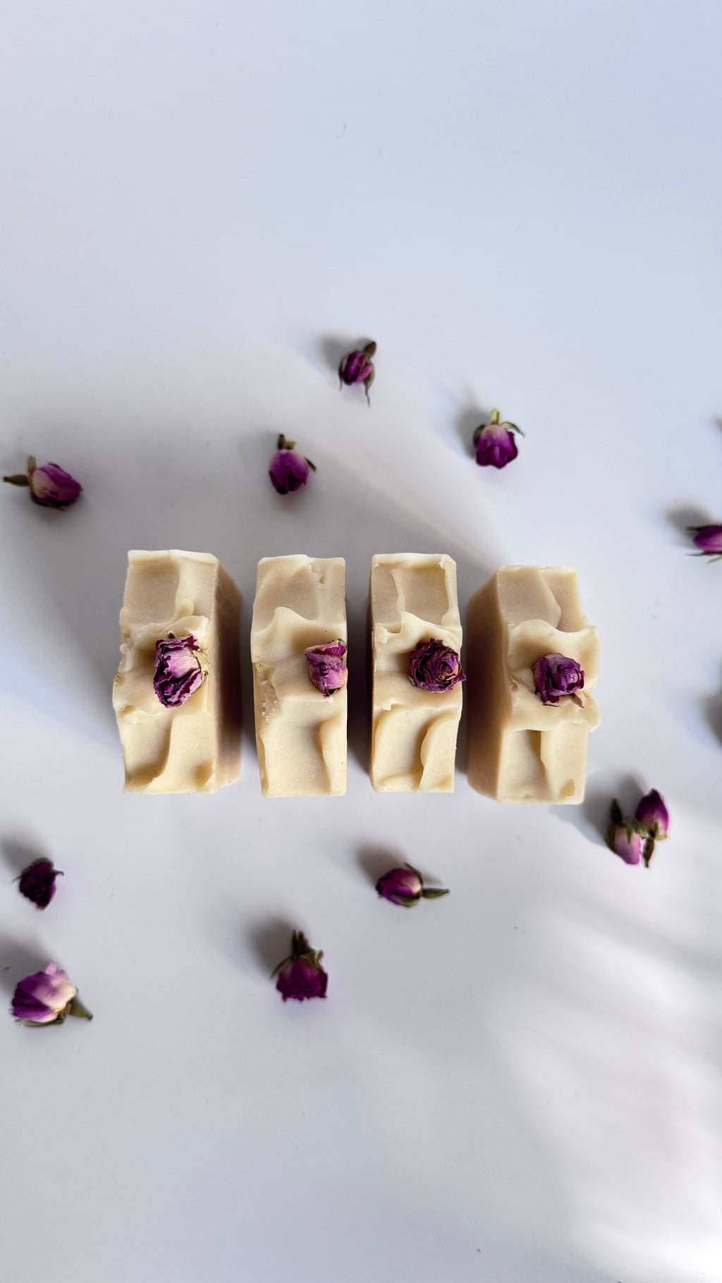 Four white beige cream coconut milk natural soap bars with dried pink roses on a white surface 