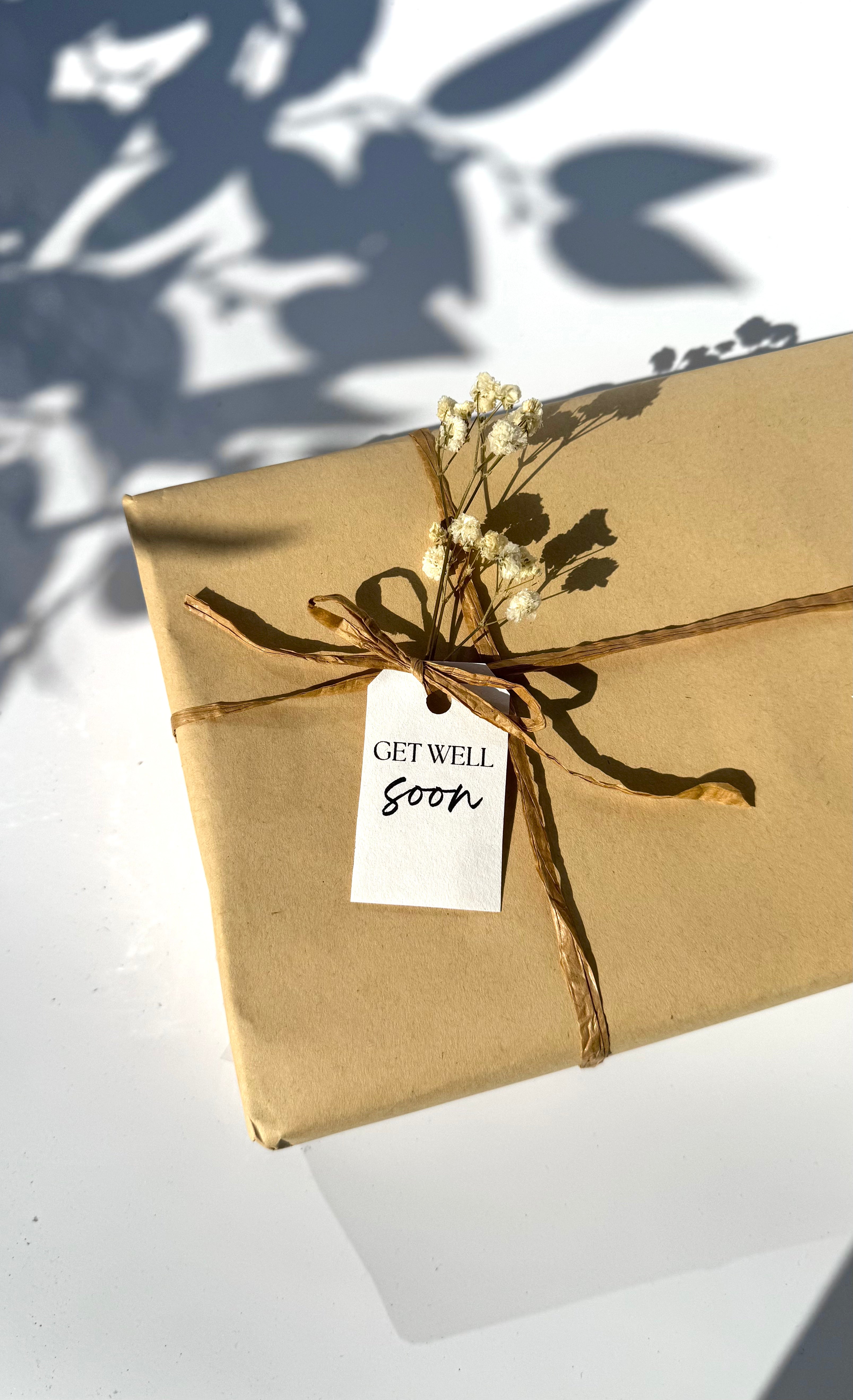 Gift wrapped in brown paper with a 'Get Well Soon' tag on a white surface.