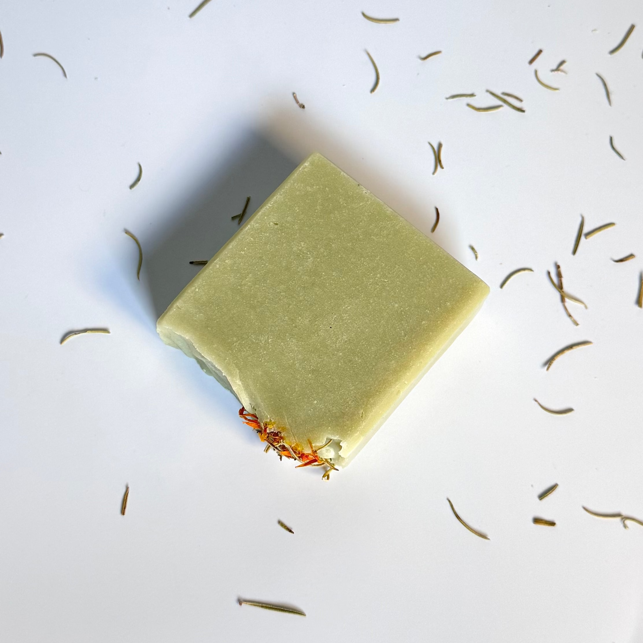 Above view of green rosemary cedarwood natural soap bar above view flat with dried floral botanical elements on a light background.
