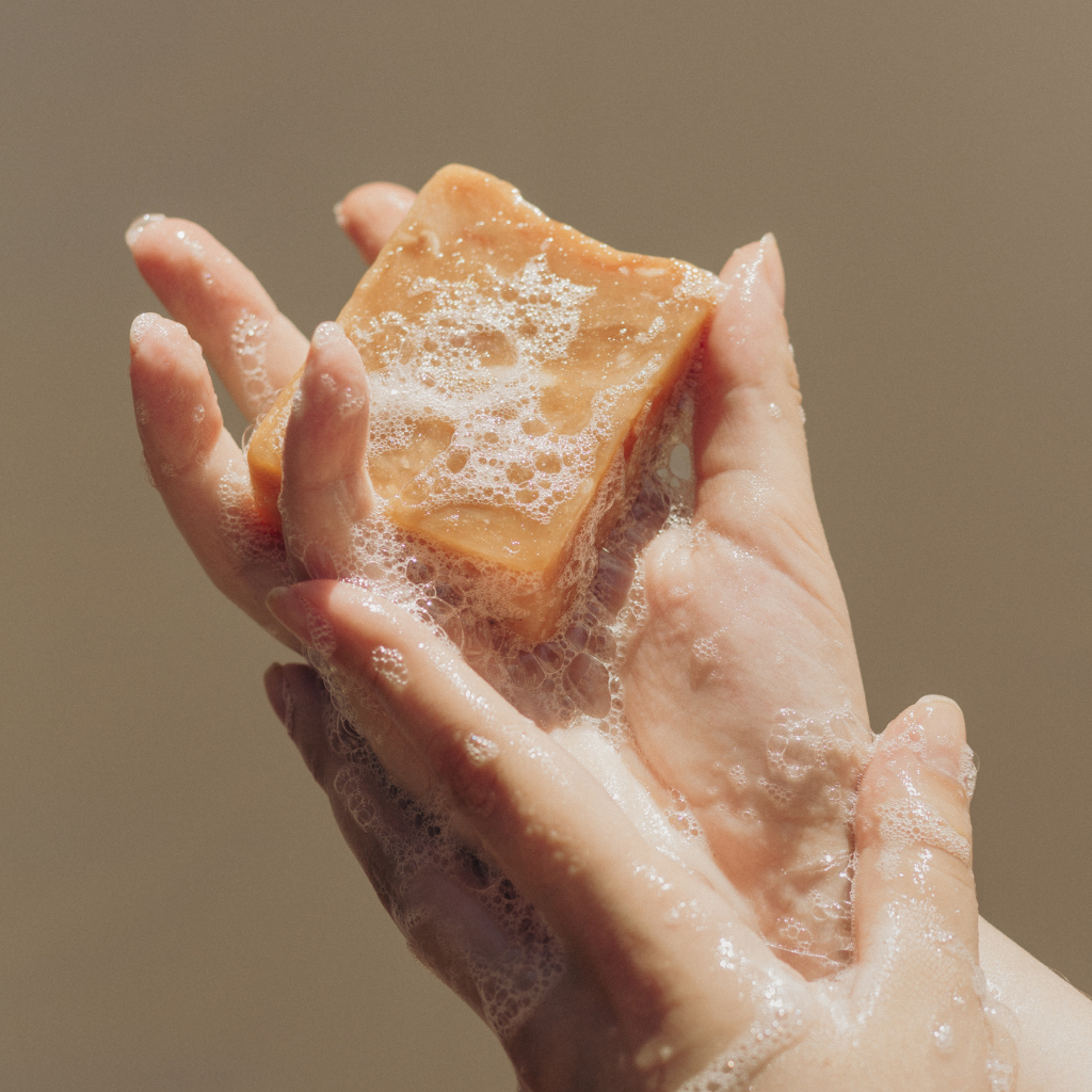 Hand holding a bar of soap with lather against a neutral background