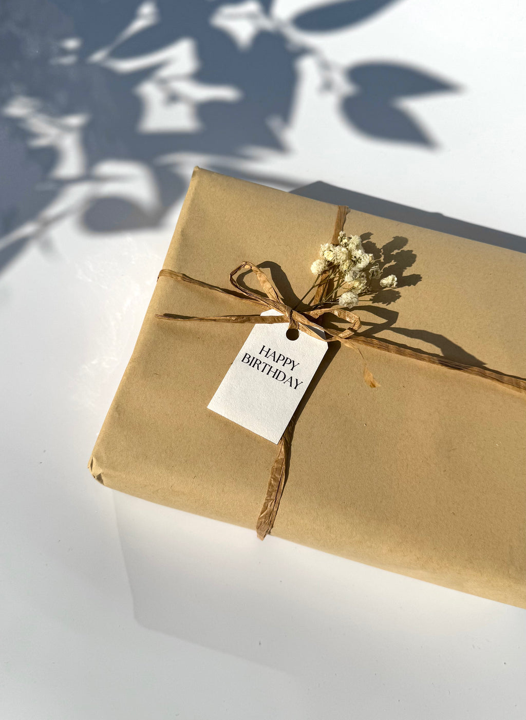 Gift wrapped in brown paper with a 'Happy Birthday' tag on a white surface.