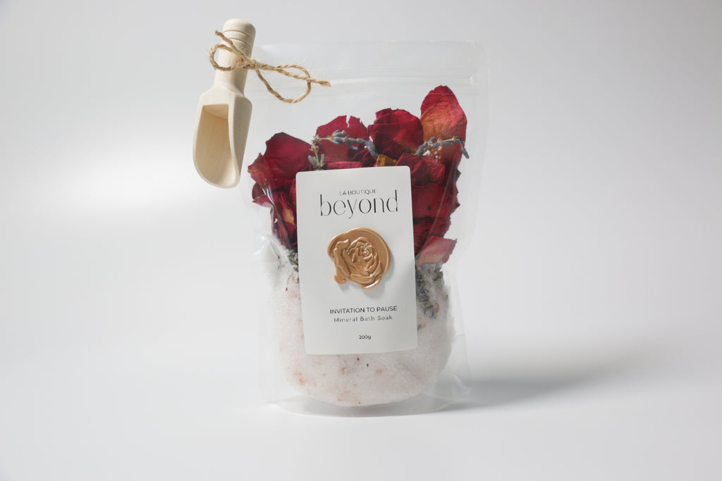 Pouch of natural bath soak, Epsom salt Himalayan pink salt with dried red rose petals, lavender buds with 'La Boutique Beyond' label on a white background
