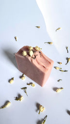 Pink chamomile rose geranium natural soap bar above view with dried jasmine flowers on a light gray background