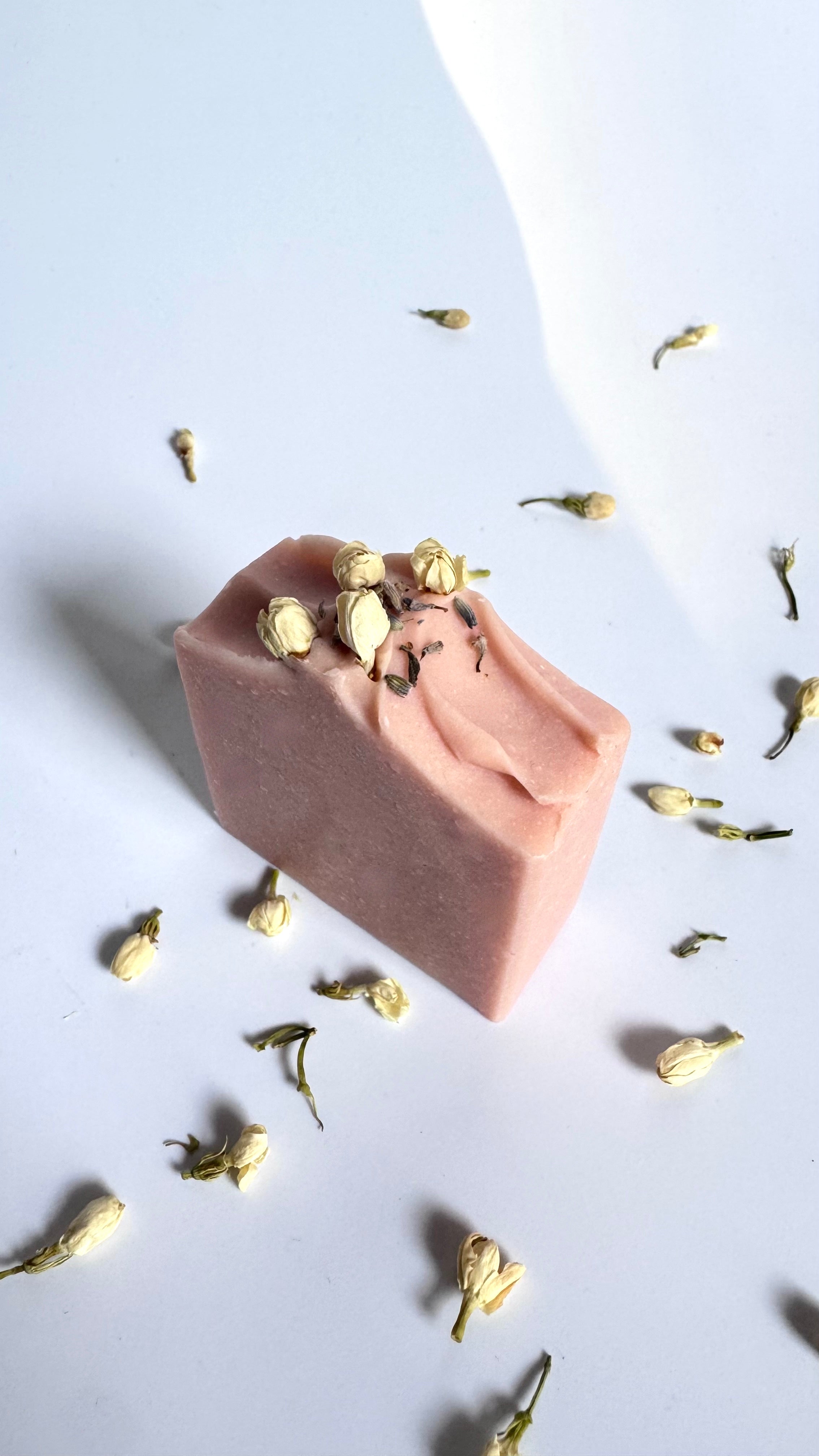Pink chamomile rose geranium natural soap bar above view with dried jasmine flowers on a light gray background