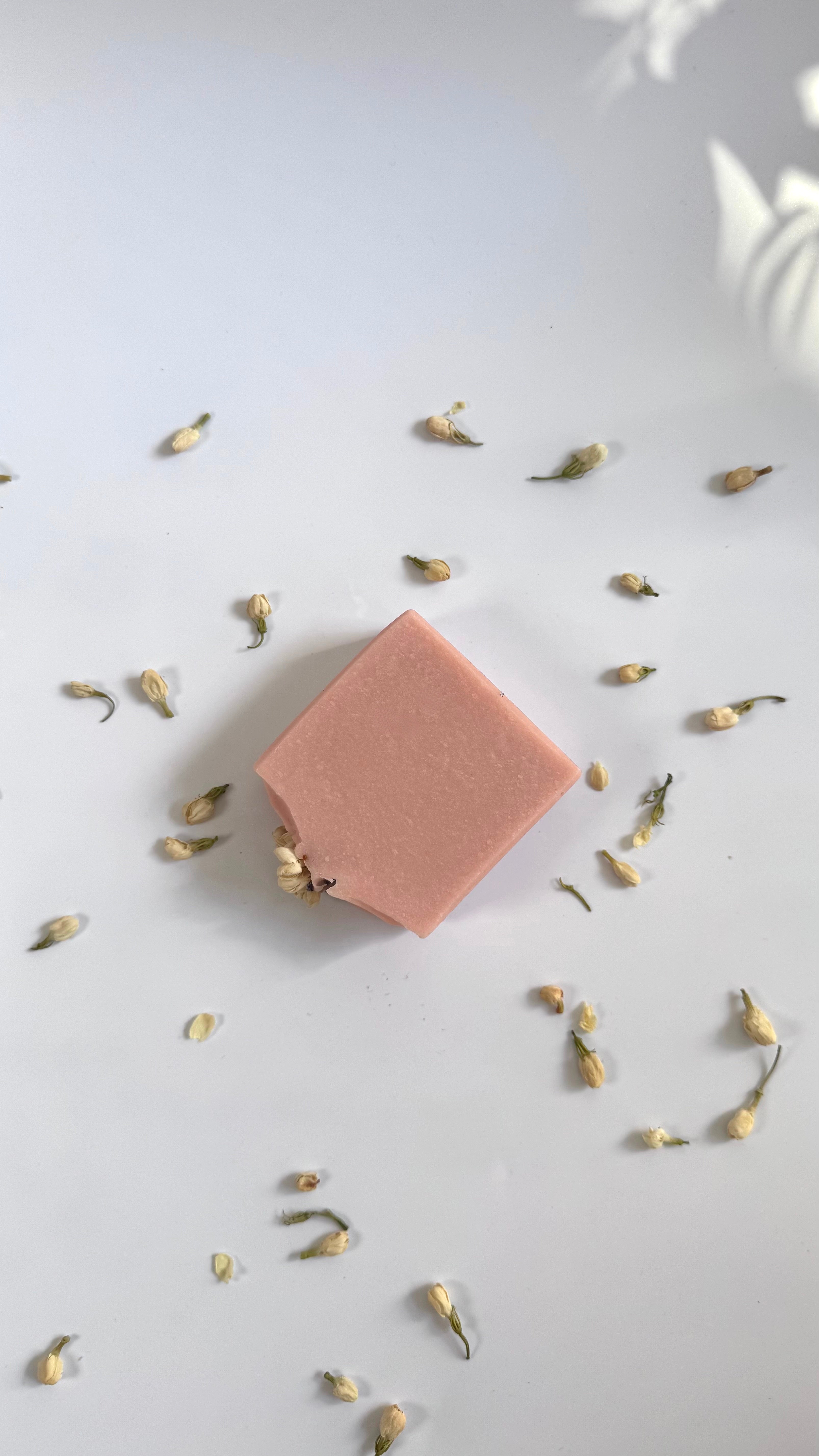 Pink chamomile rose geranium natural soap bar flat above view with dried jasmine flowers on a light gray background