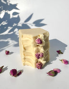 Stack of four white beige cream coconut milk natural soaps bars with dried pink roses on a white surface with shadow leaves