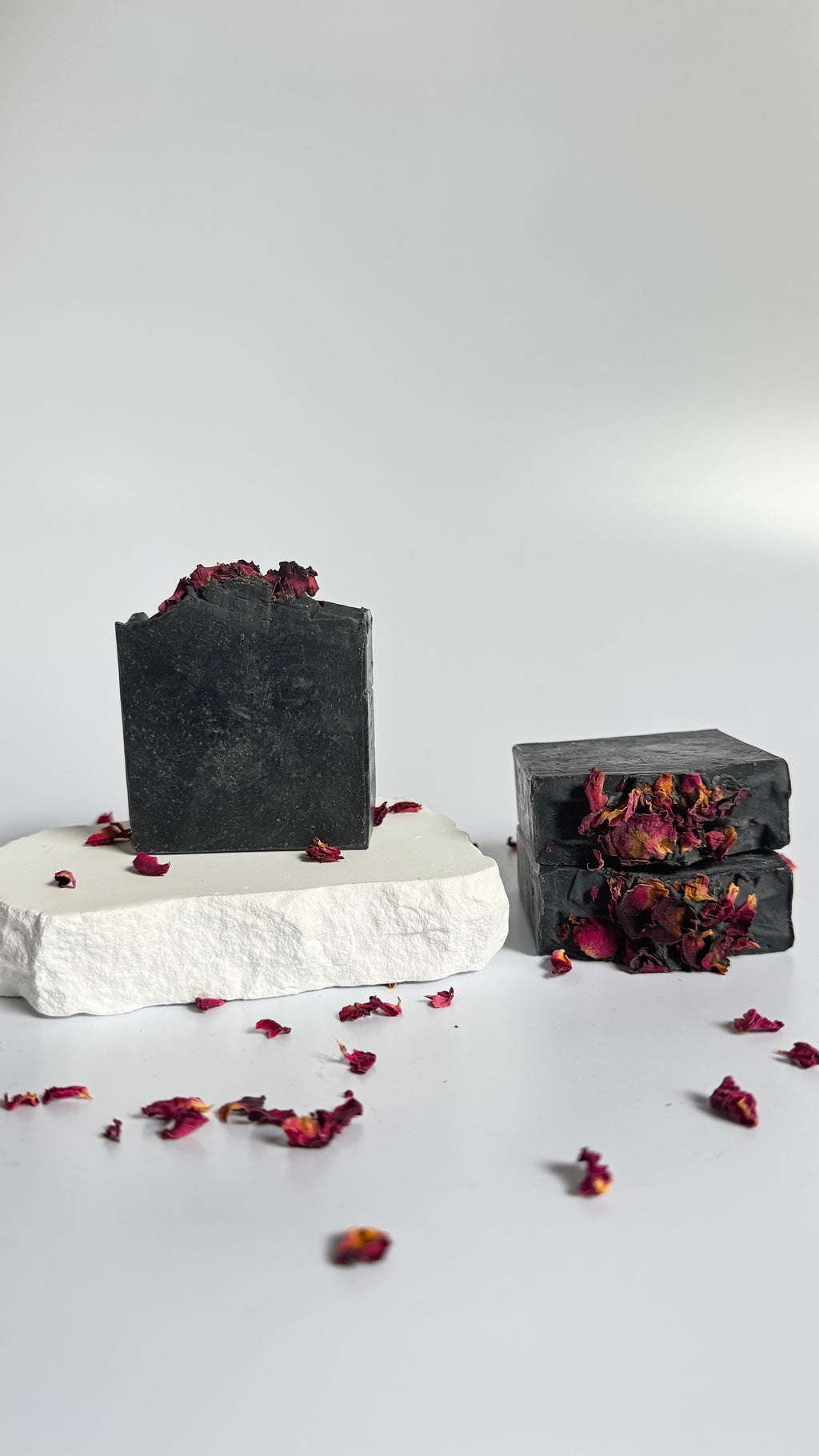 Stack of three black activated charcoal lavender tea tree natural soap bar with dried rose petals on a white background 