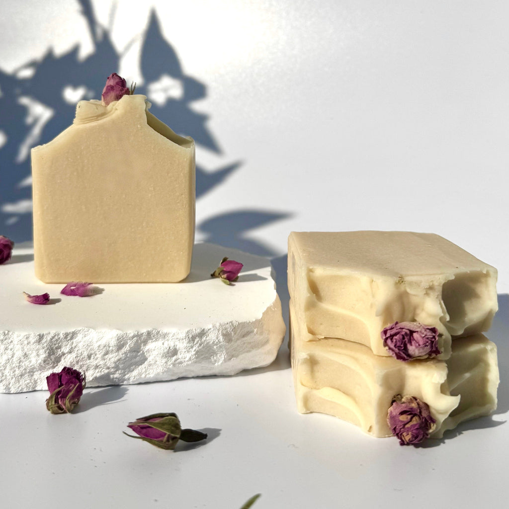 Stack of three white beige cream coconut milk natural soap bars with dried pink roses on a white surface with shadow leaves