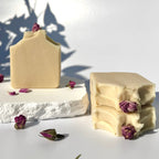 Stack of three white beige cream coconut milk natural soap bars with dried pink roses on a white surface with shadow leaves