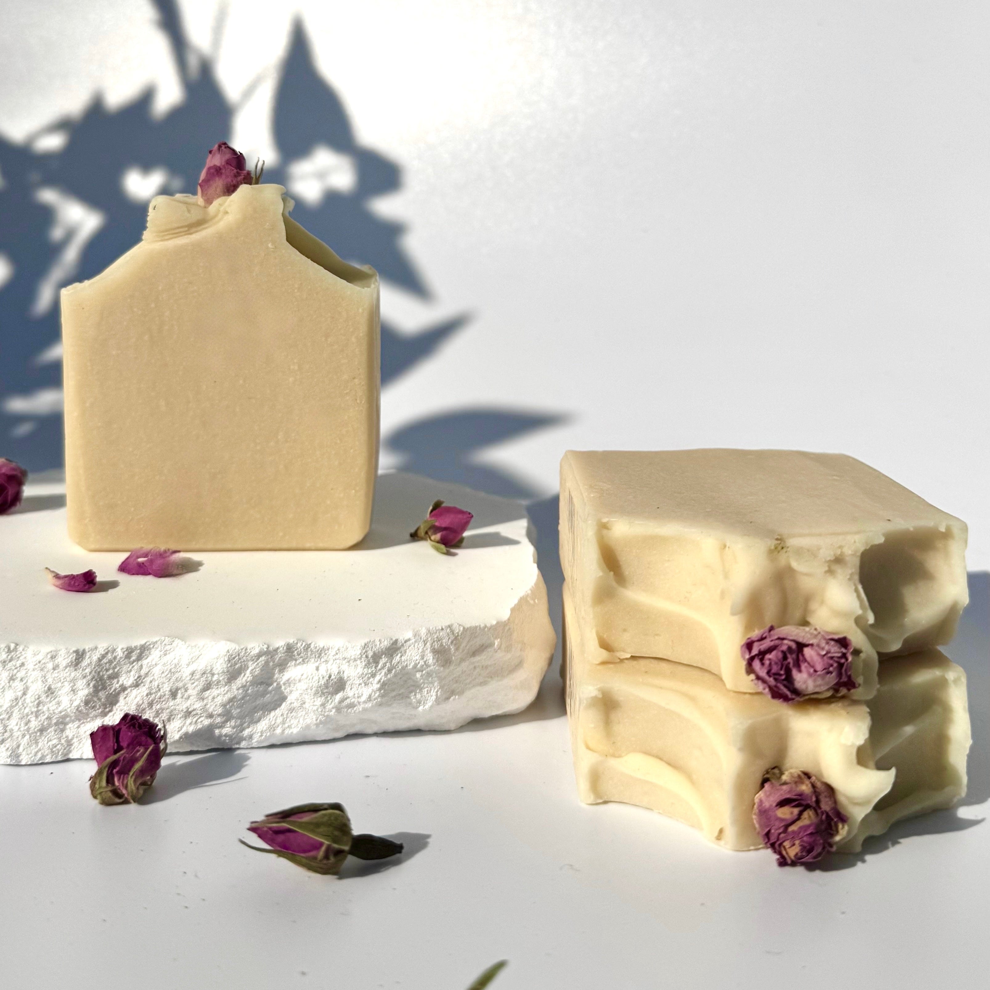 Stack of three white beige cream coconut milk natural soap bars with dried pink roses on a white surface with shadow leaves