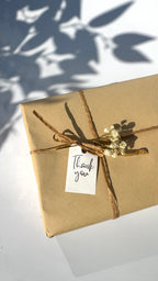 Gift wrapped in brown paper with a decorative bow and 'Thank you' tag on a light background.