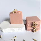 Stack of three pink chamomile rose geranium natural soap bars with dried jasmine flowers on a light gray background