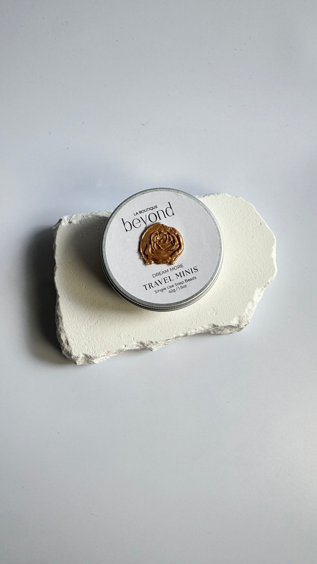 Tin of mini travel soap beads and a packaging box labeled 'La Boutique Beyond' on a light background.