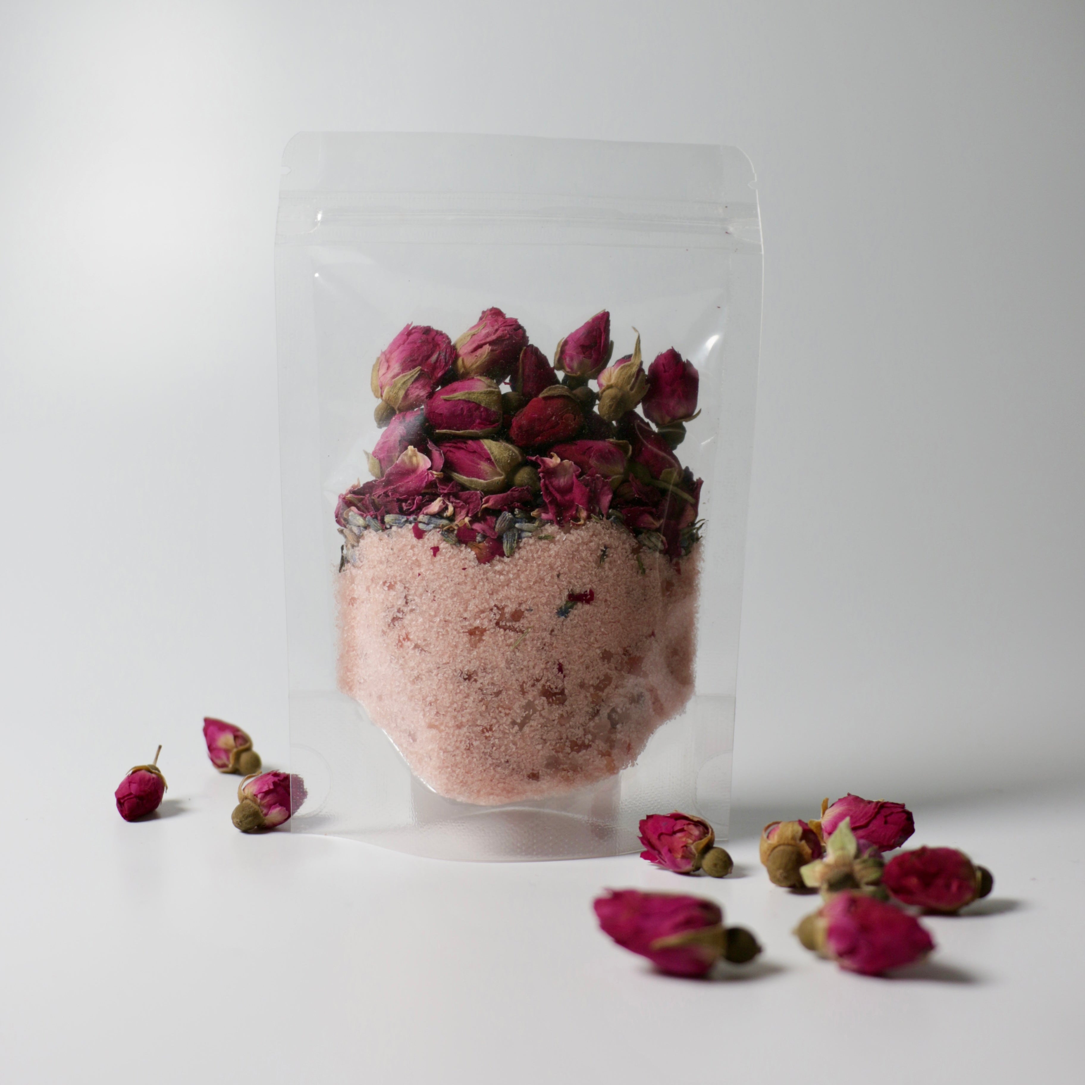 Clear plastic bag with pink bath salts and dried flowers on a white background