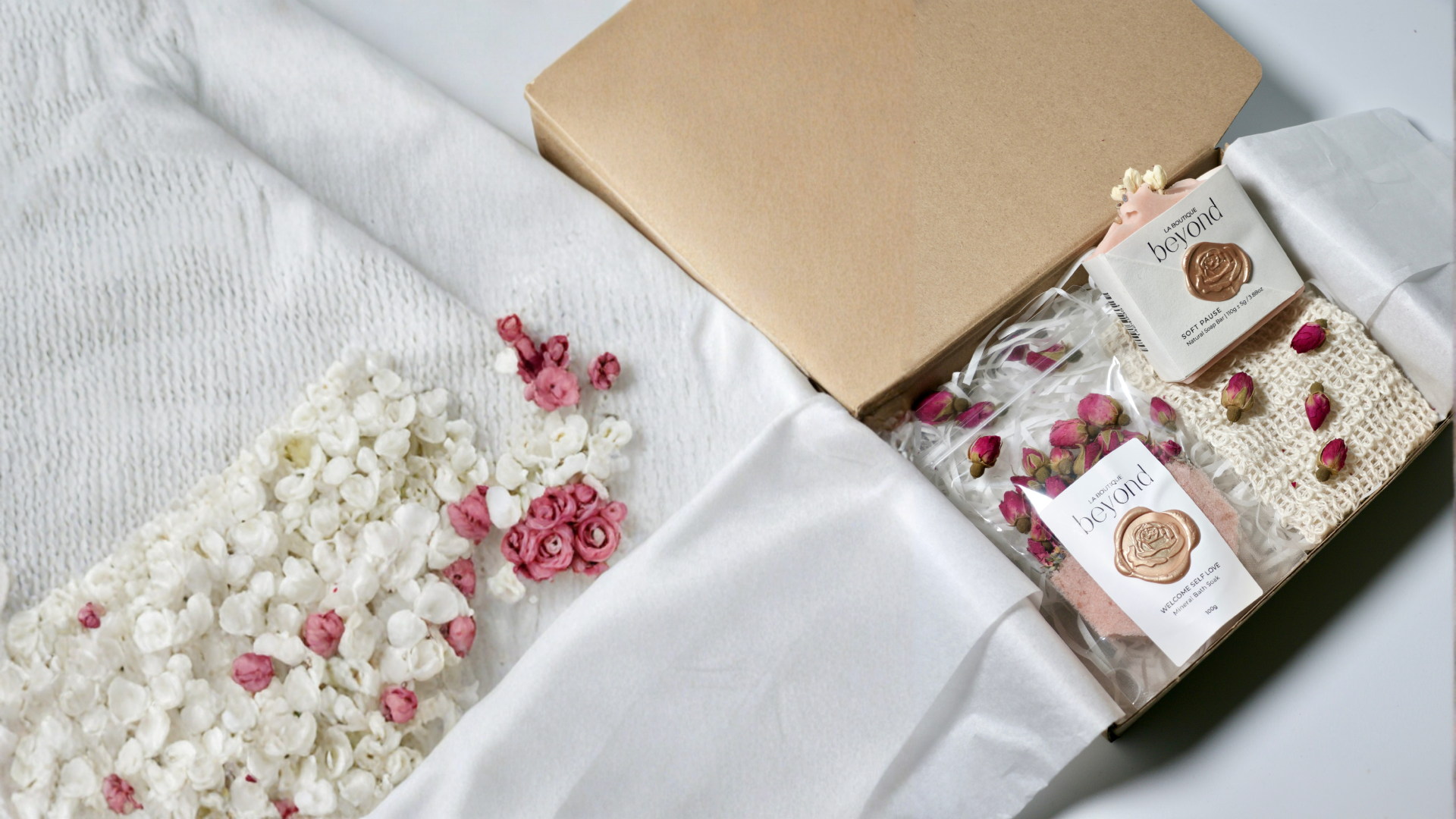 Valentine's Day gift box with natural soap bars and bath soaks and flowers on a white surface