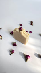 Side view of white beige cream coconut milk natural soap bar with dried pink roses on a white surface with shadow leaves