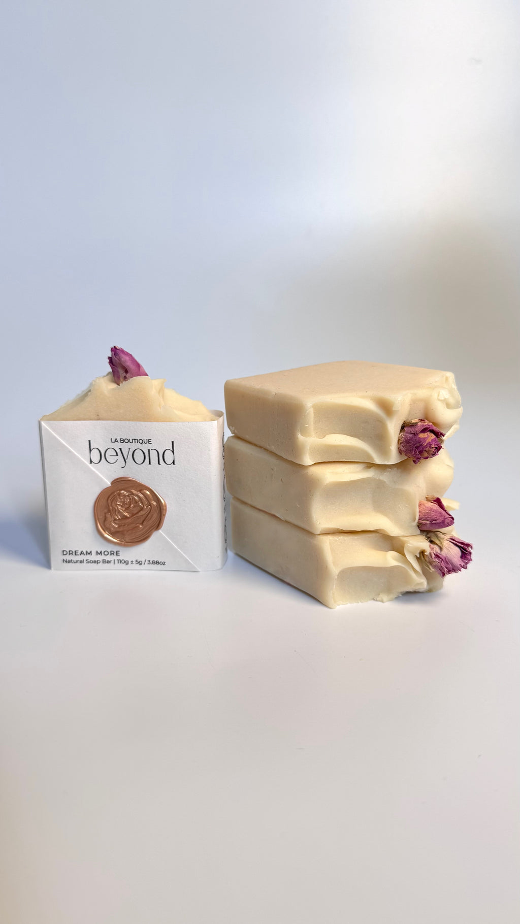 White beige cream coconut milk natural soap bars with dried pink roses on a white surface and a packaging box labeled 'La Boutique Beyond' on a light background.