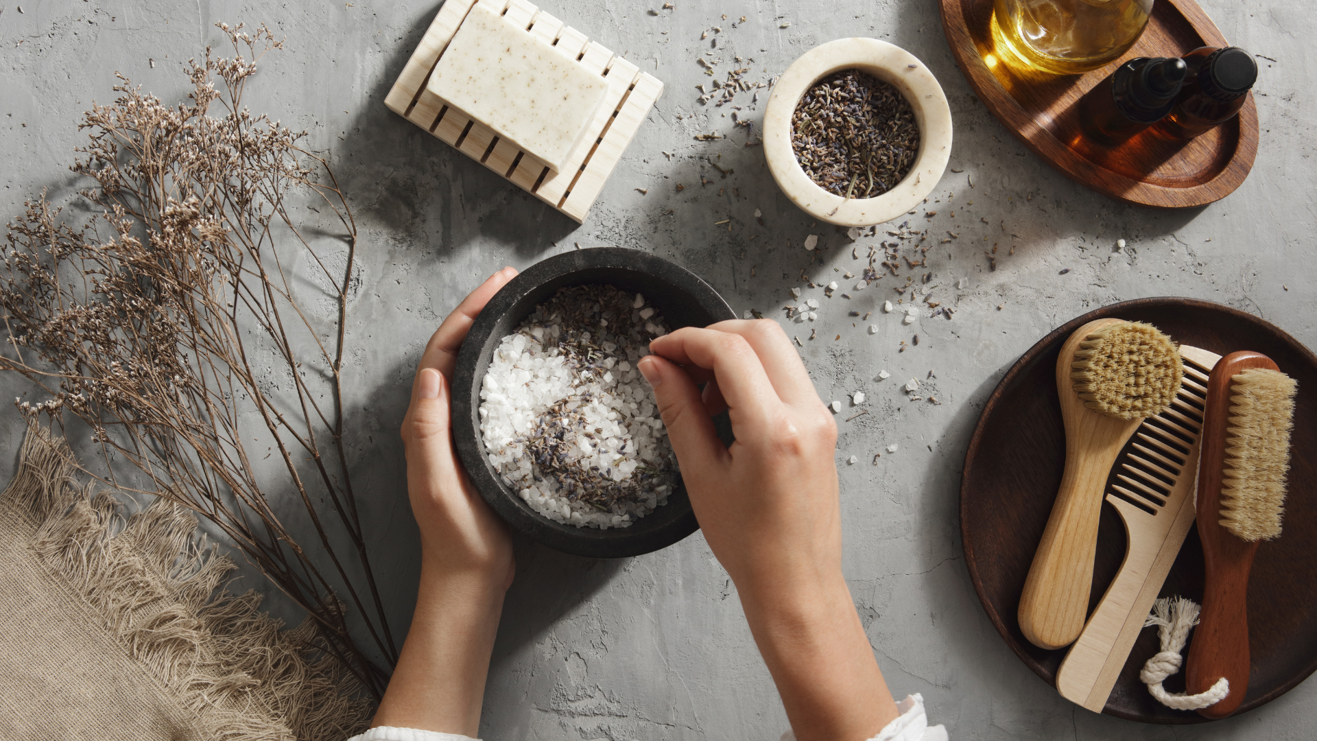 Person preparing a natural bath soak product with ingredients on a gray surface
