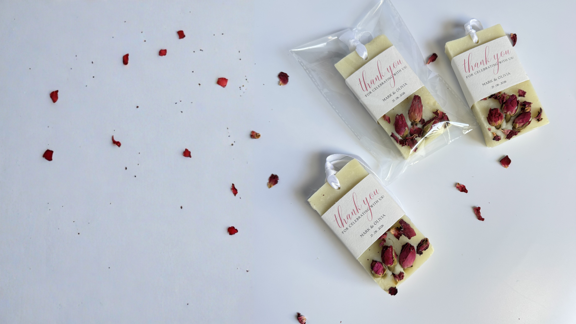 Three small packages of custom gift soap favors for celebrations, weddings and corporate events with personalised message and dried rose petals on a light gray background