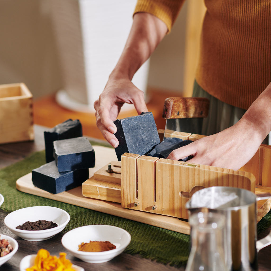 Person arranging soap bars on a wooden soap dish with a blurred background