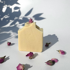 White beige cream coconut milk natural soap bar with dried pink roses on a white surface with shadow leaves